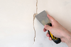 A close-up photograph of a crack in a wall, showing signs of structural damage and potential water leakage.